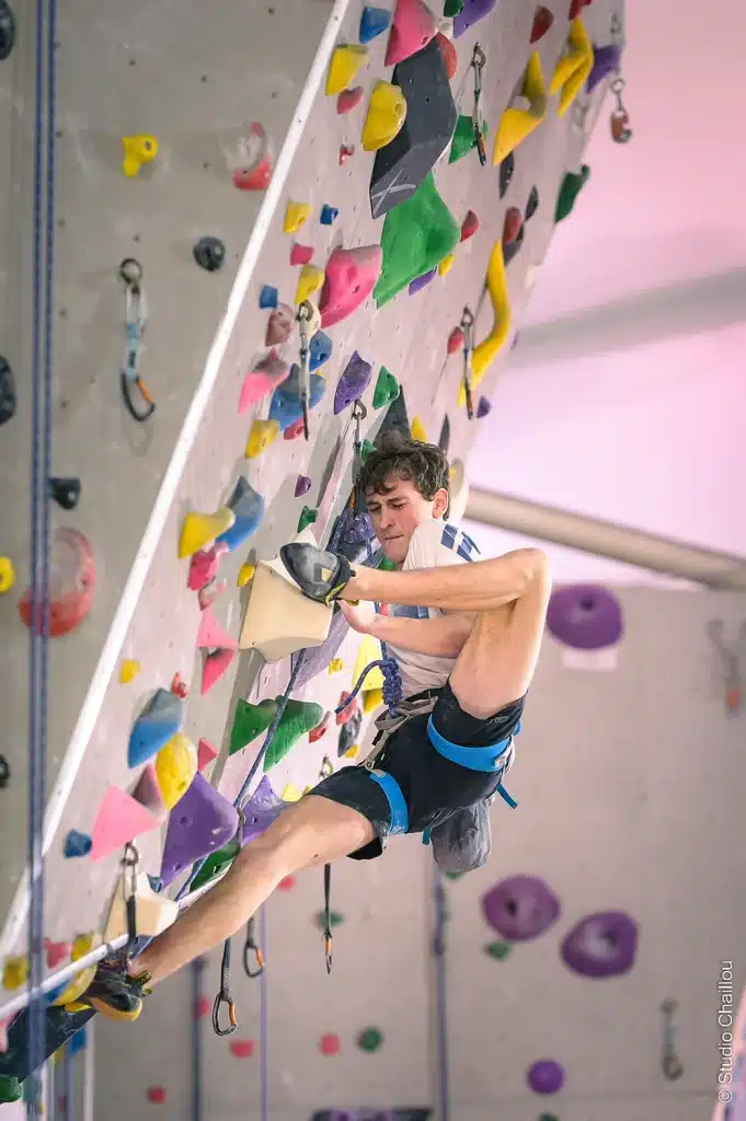 Grimpeur en compétition d'escalade en salle s'agrippant à une prise sur mur déversant, reportage photo sportif — Studio Chaillou Lyon
