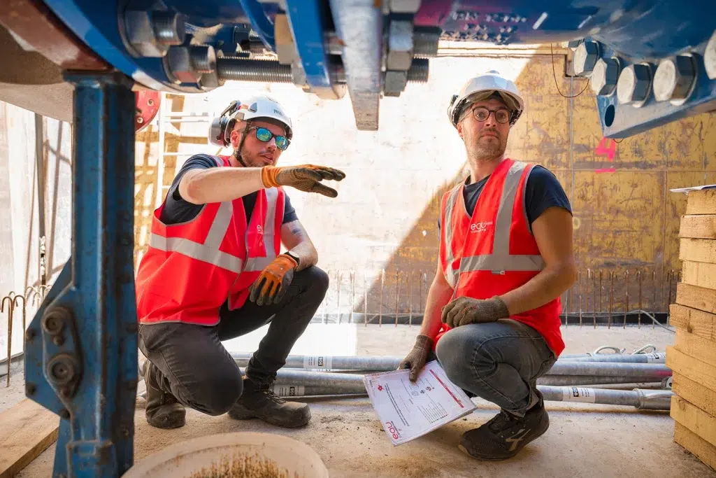Deux techniciens BTP en équipements de protection sur un chantier à Lyon, échangeant sur les plans d'exécution — reportage photo chantier Studio Chaillou